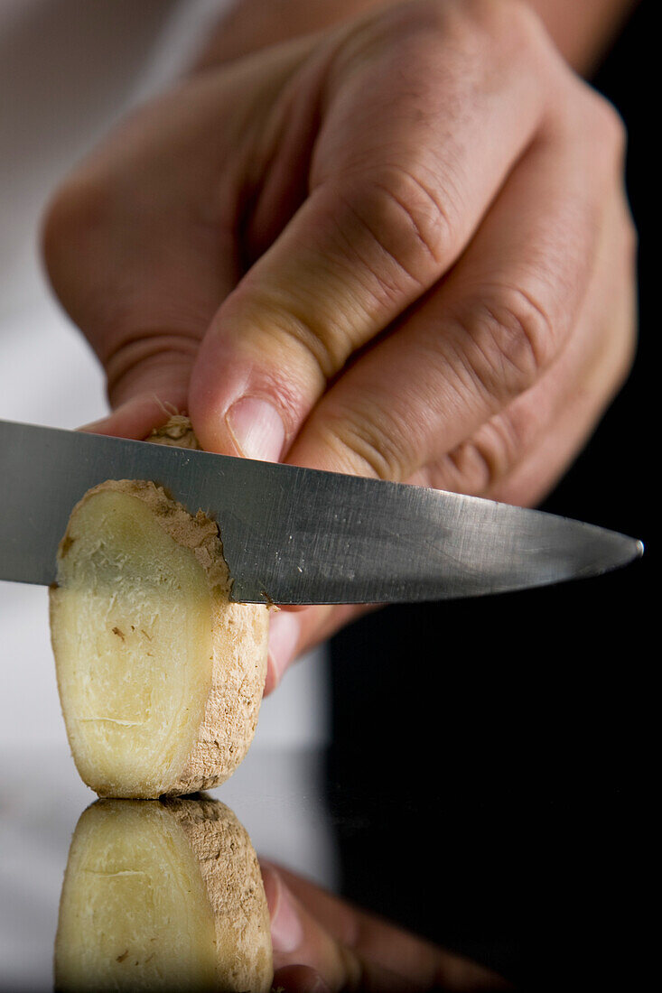 Close up of a chef hand slicing ginger