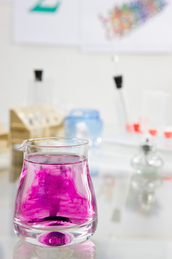 Close up of a glass container filled with  fluid and dark pink chemical solution