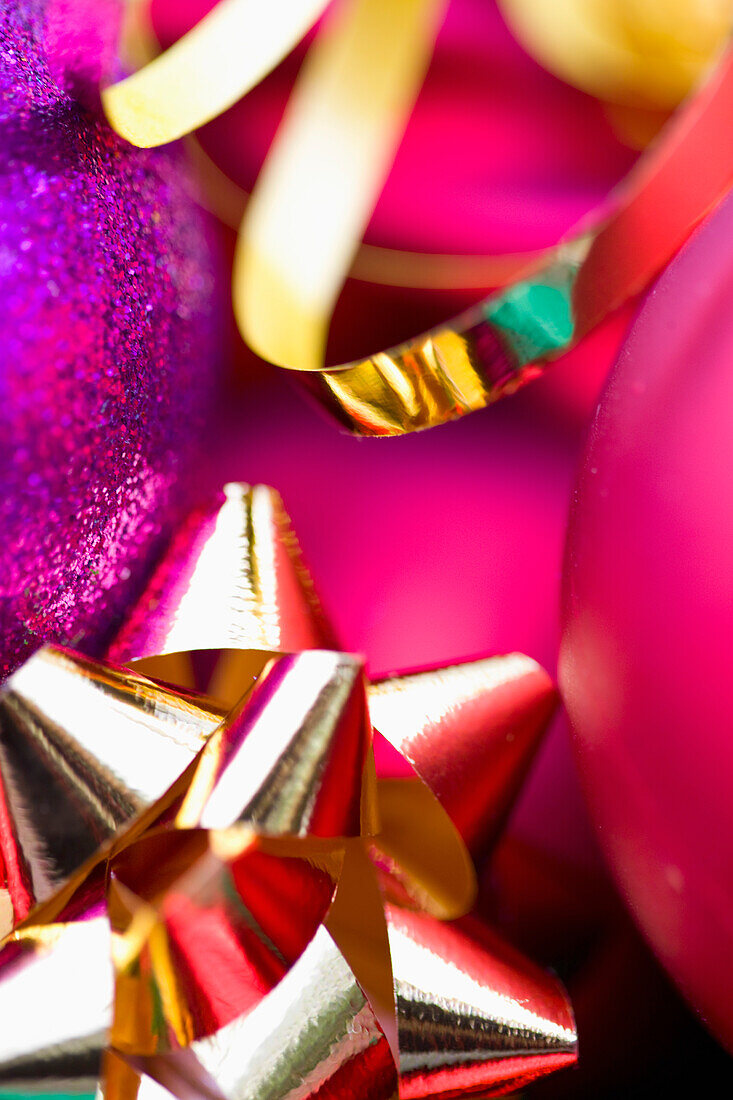 Extreme close up of red and purple Christmas baubles and a gold bow and ribbon