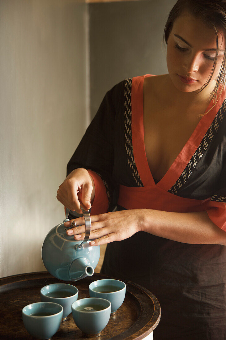 Young woman holding teapot and pouring green tea