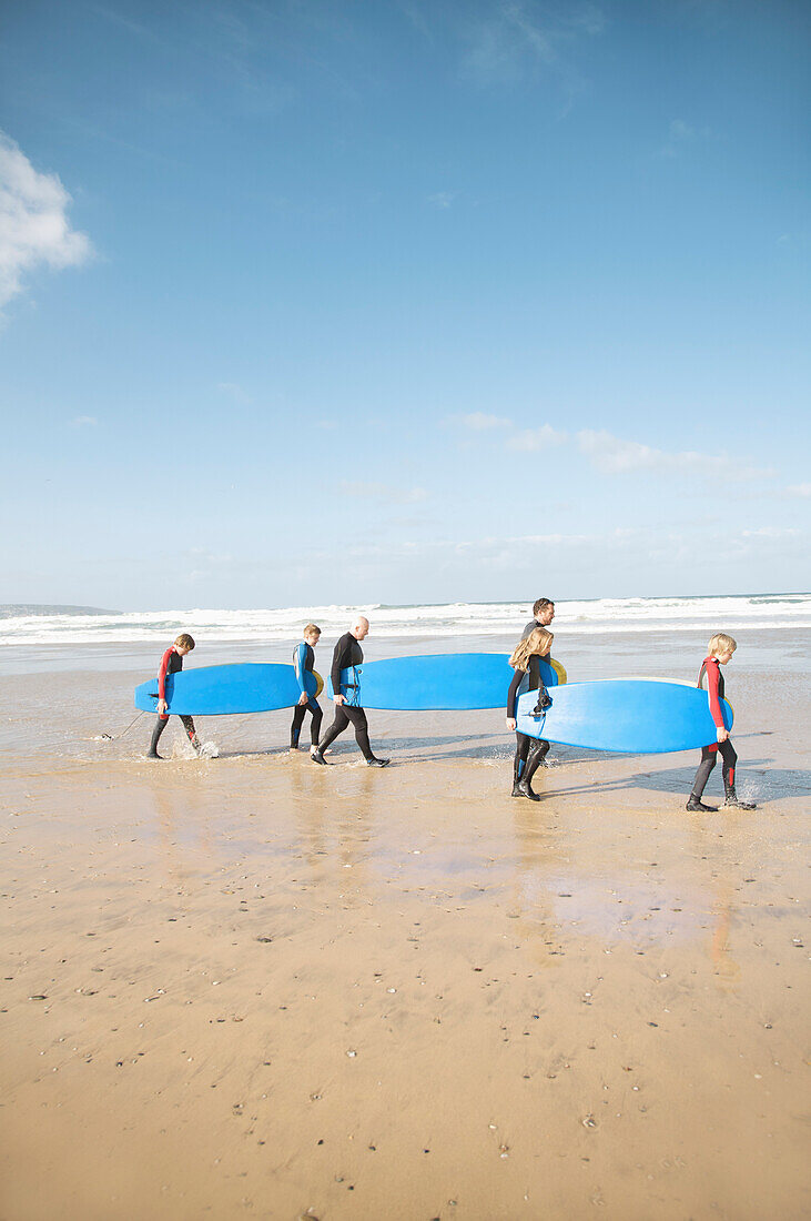 Men and children walking on a beach carrying surfboards