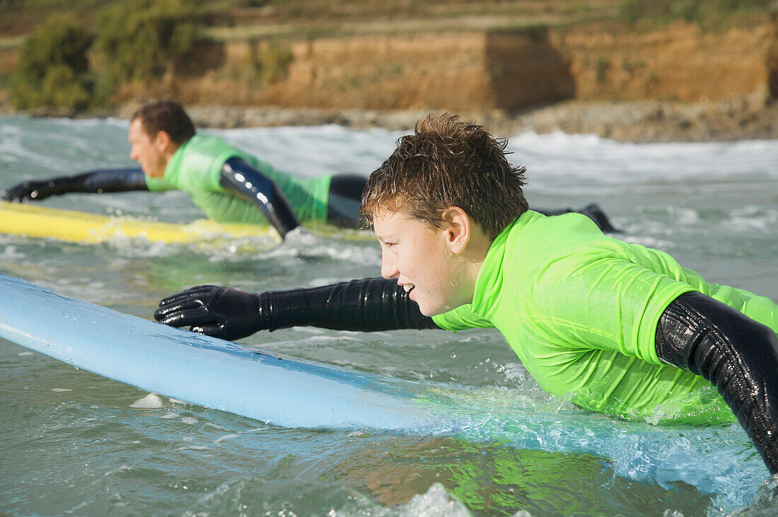 Jugendlicher Junge auf seinem Surfbrett liegend beim Paddeln