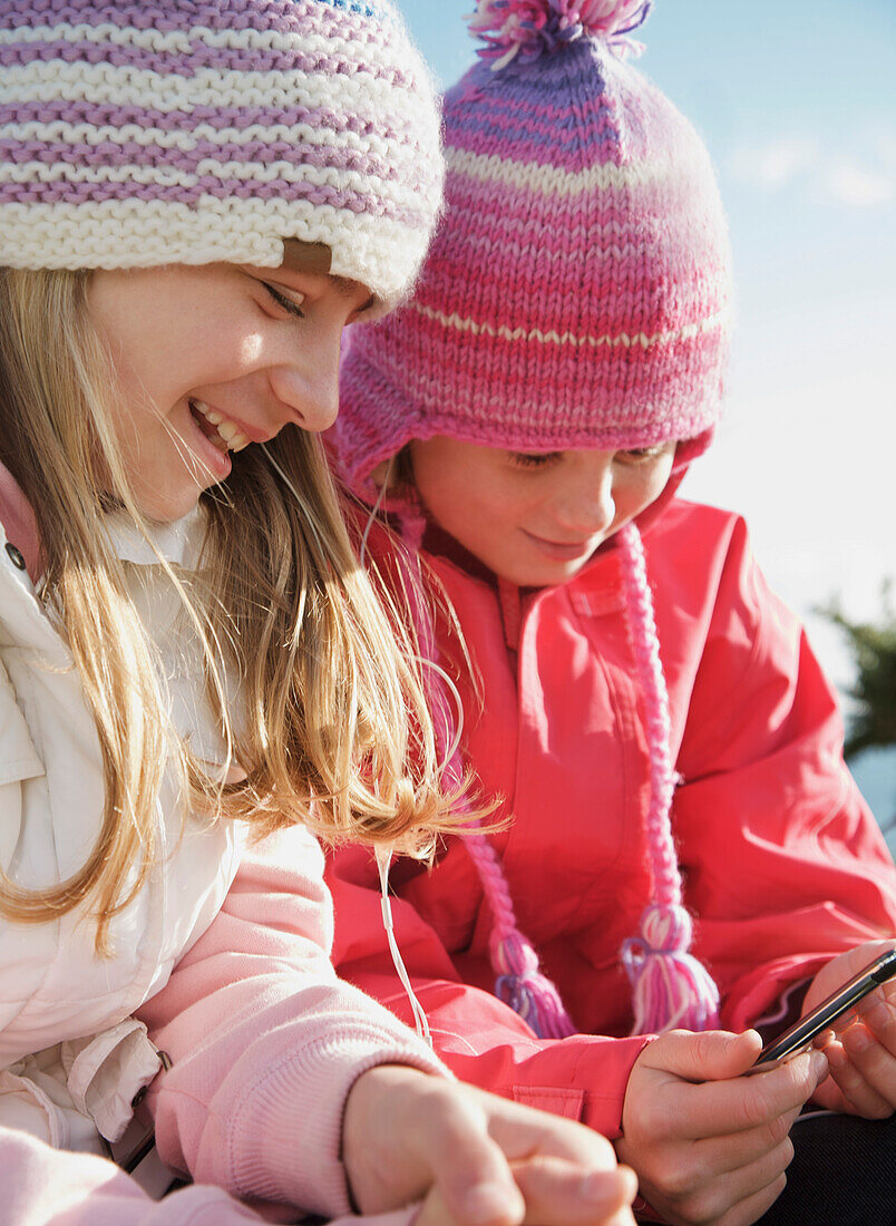 Two young girls wearing woolly hats and holding a mp3 player
