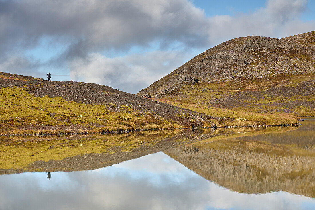 Menschen stehen auf den vulkanischen Felsen mit ihrer Spiegelung in einem See am Valafell-Pass, in der Nähe von Olafsvik, Snaefellsnes-Halbinsel, Westküste Islands; Island