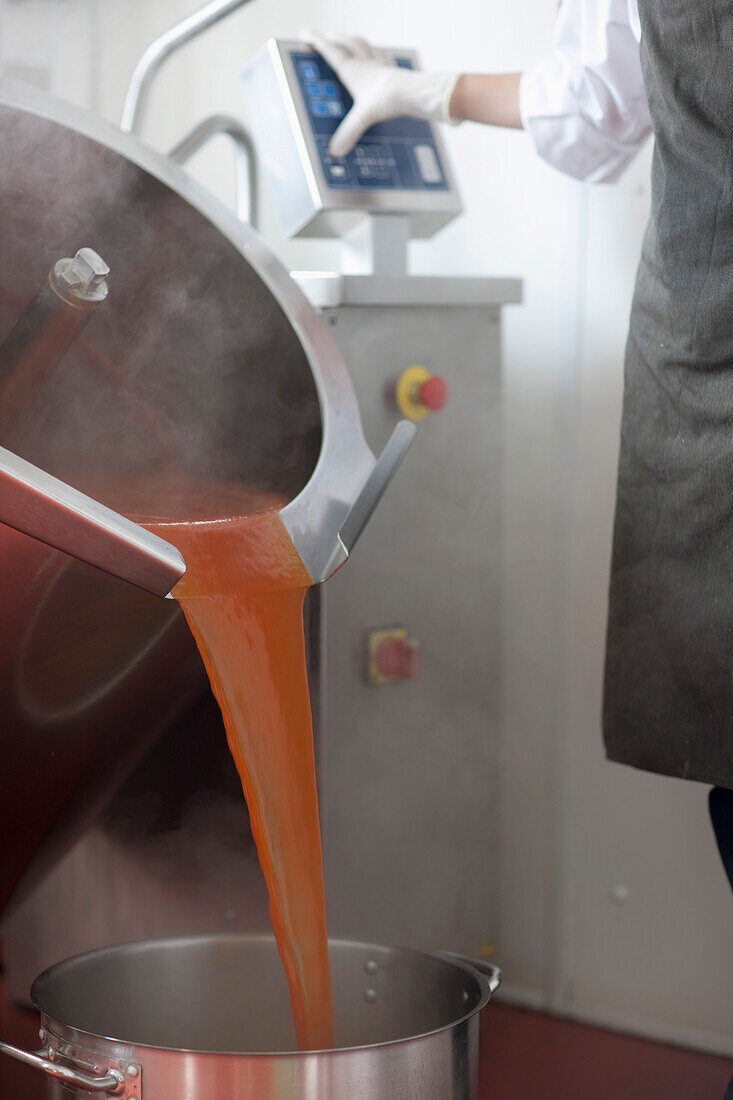 Fabrikarbeiter gießt mit Hilfe computergesteuerter Maschinen Tomatensoße in einen Topf