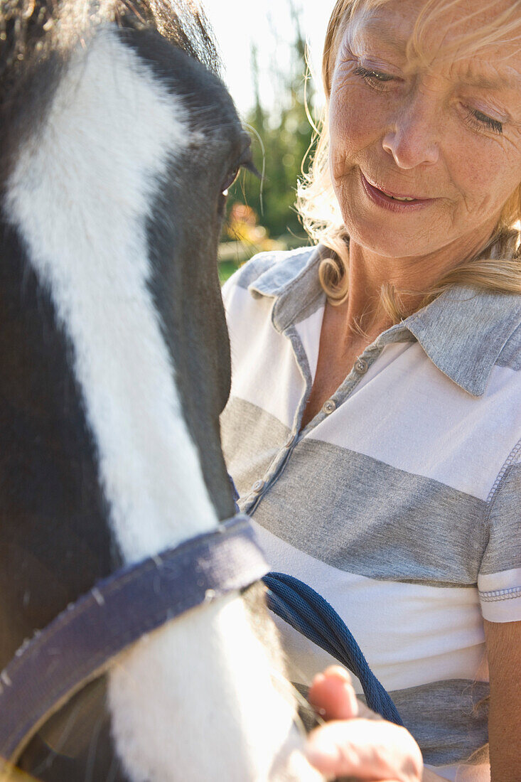 Reife Frau steht neben einem Pferd