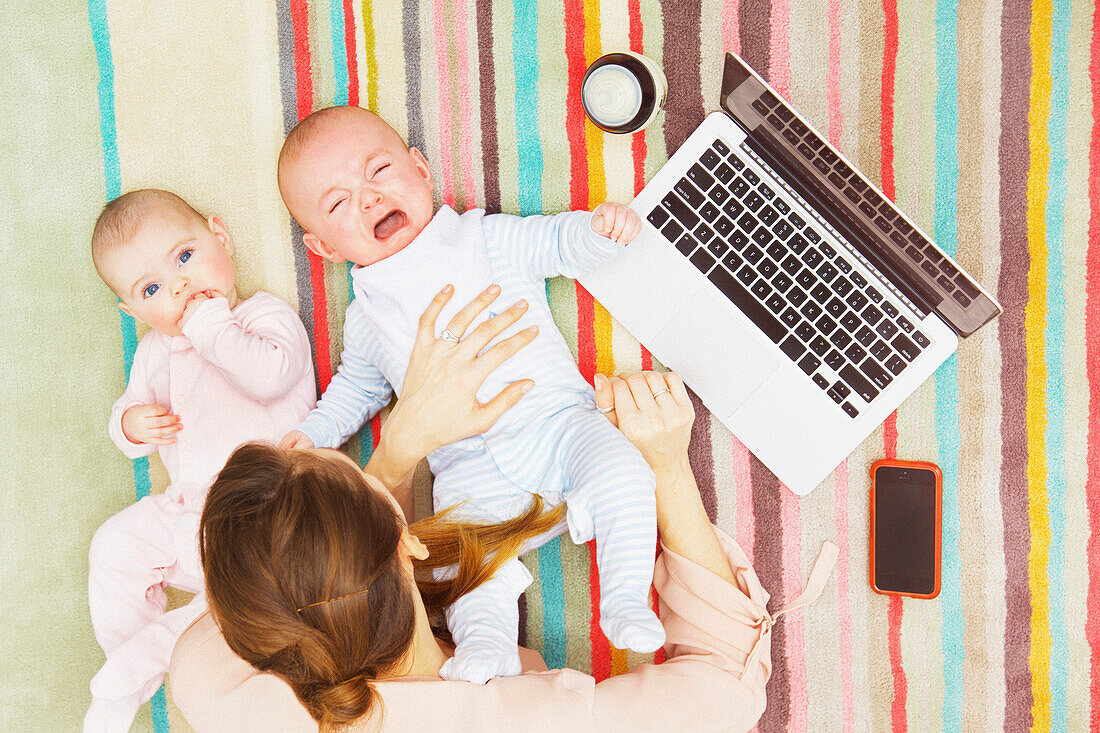 Mutter mit Zwillingsbabys auf dem Boden liegend mit Laptop, erhöhte Ansicht