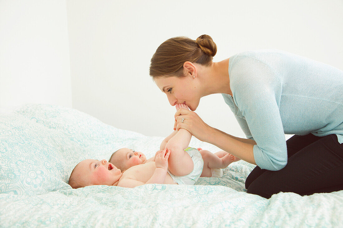 Mother Kneeling on Bed Kissing Twin Babies