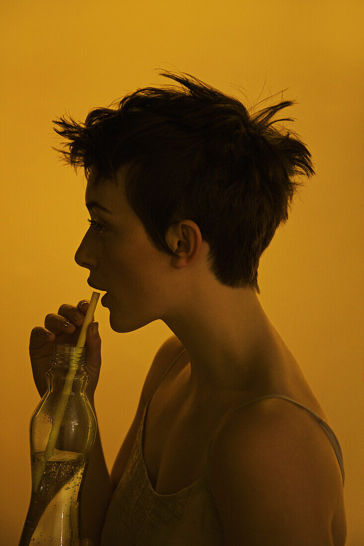 Profil einer jungen Frau, die aus einer Flasche mit Strohhalm trinkt