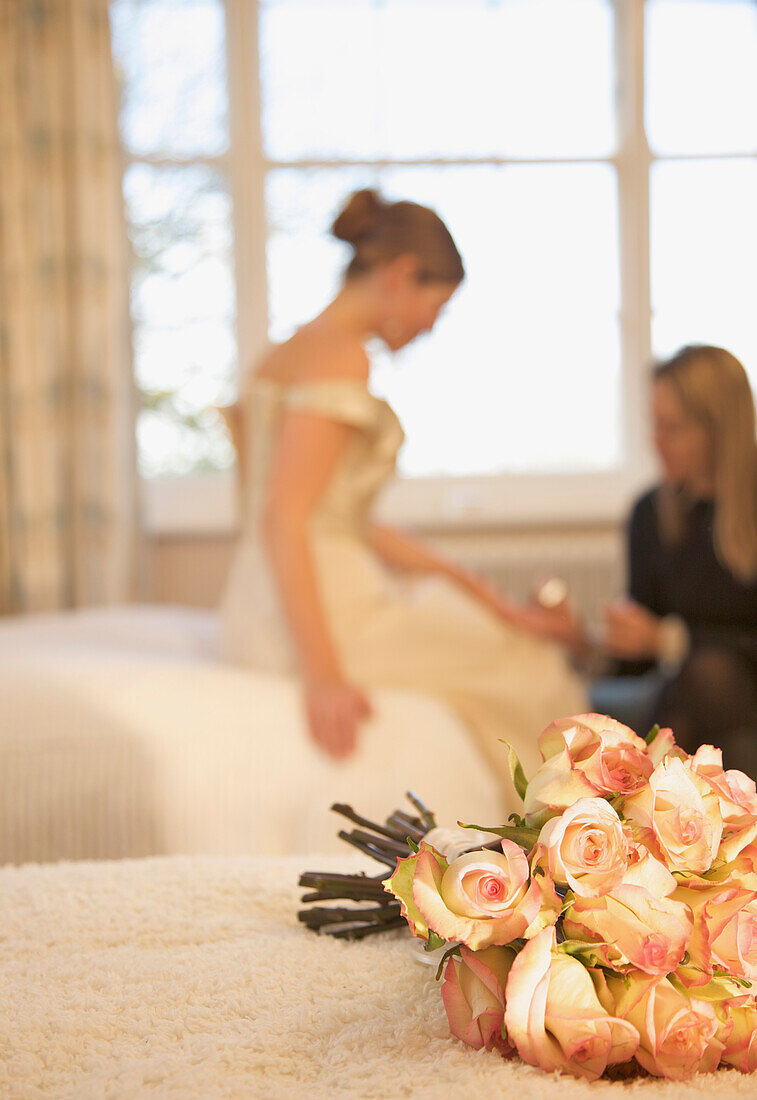 Close up of a bouquet of roses lying on a bed with bride receiving a manicure