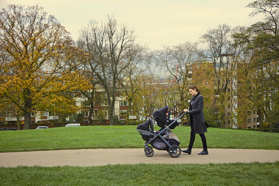 Mutter schiebt doppelten Kinderwagen im Stadtpark