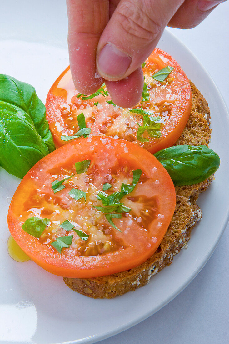 Man's Hands Adding Salt to Basil and Tomatoes Sandwich