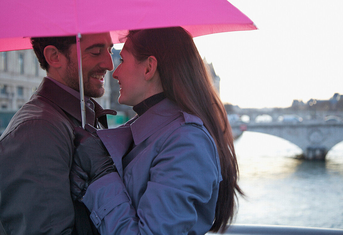 Nahaufnahme eines sich umarmenden Paares unter einem rosafarbenen Regenschirm an der Seine, Paris, Frankreich