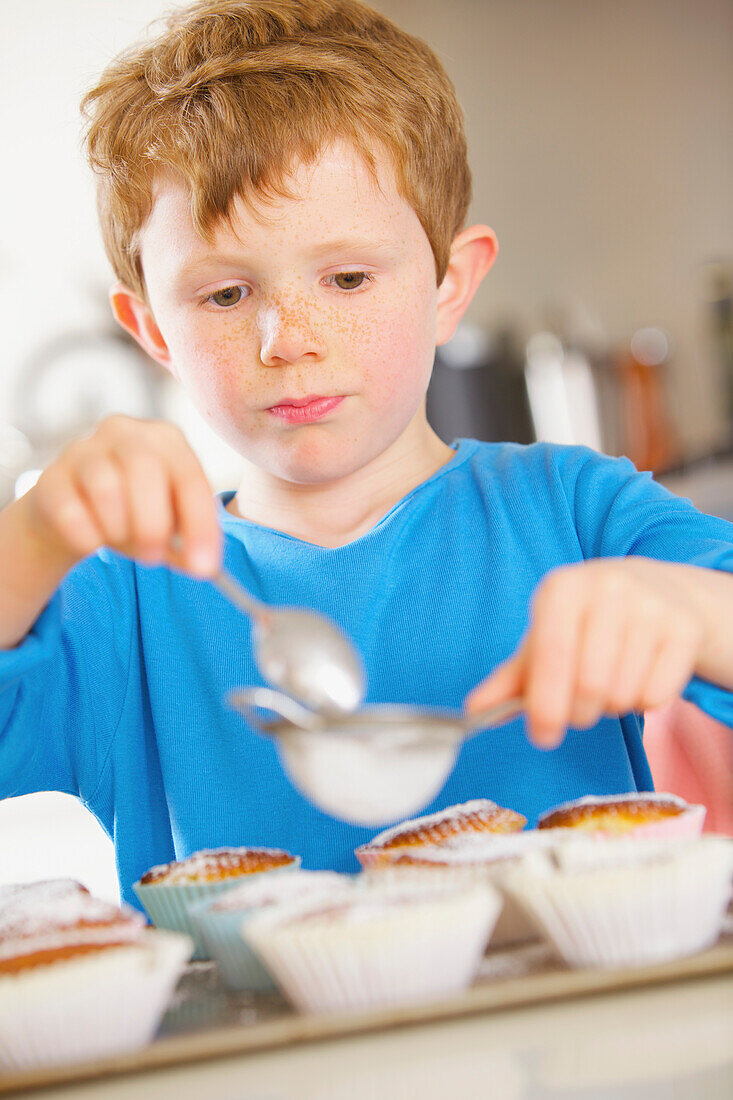 Junger Junge bestreut Muffins mit Puderzucker