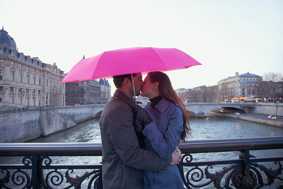 Couple kissing under a pink umbrella on a bridge over the Seine river, Paris, France