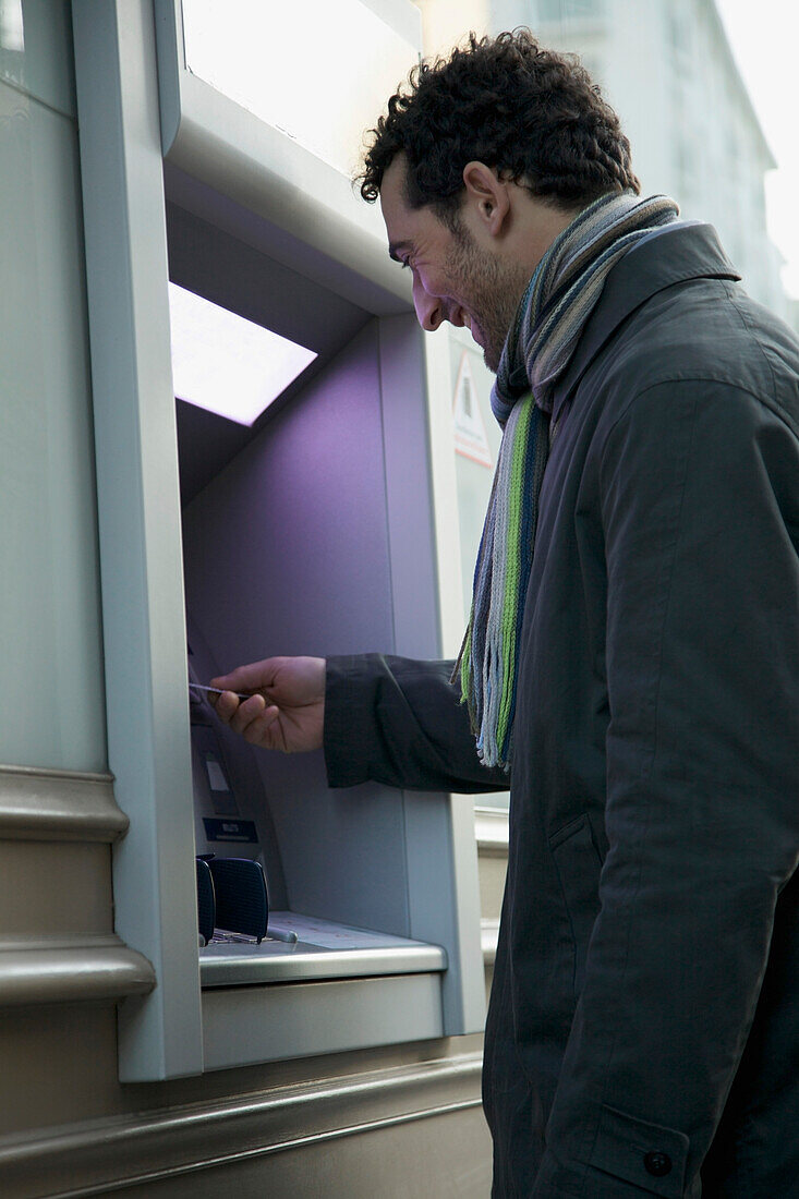 Mann im Mantel am Geldautomaten