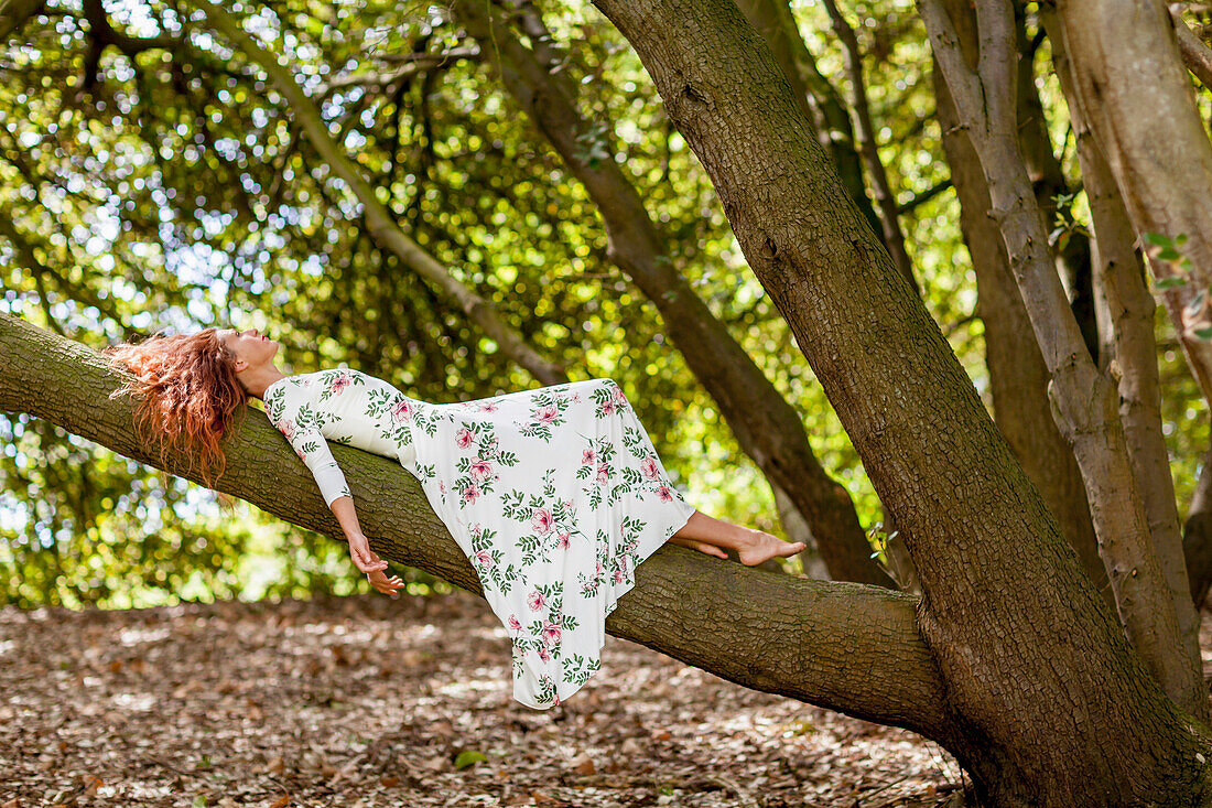 Frau in geblümtem Kleid auf einem Baumstamm im Wald liegend