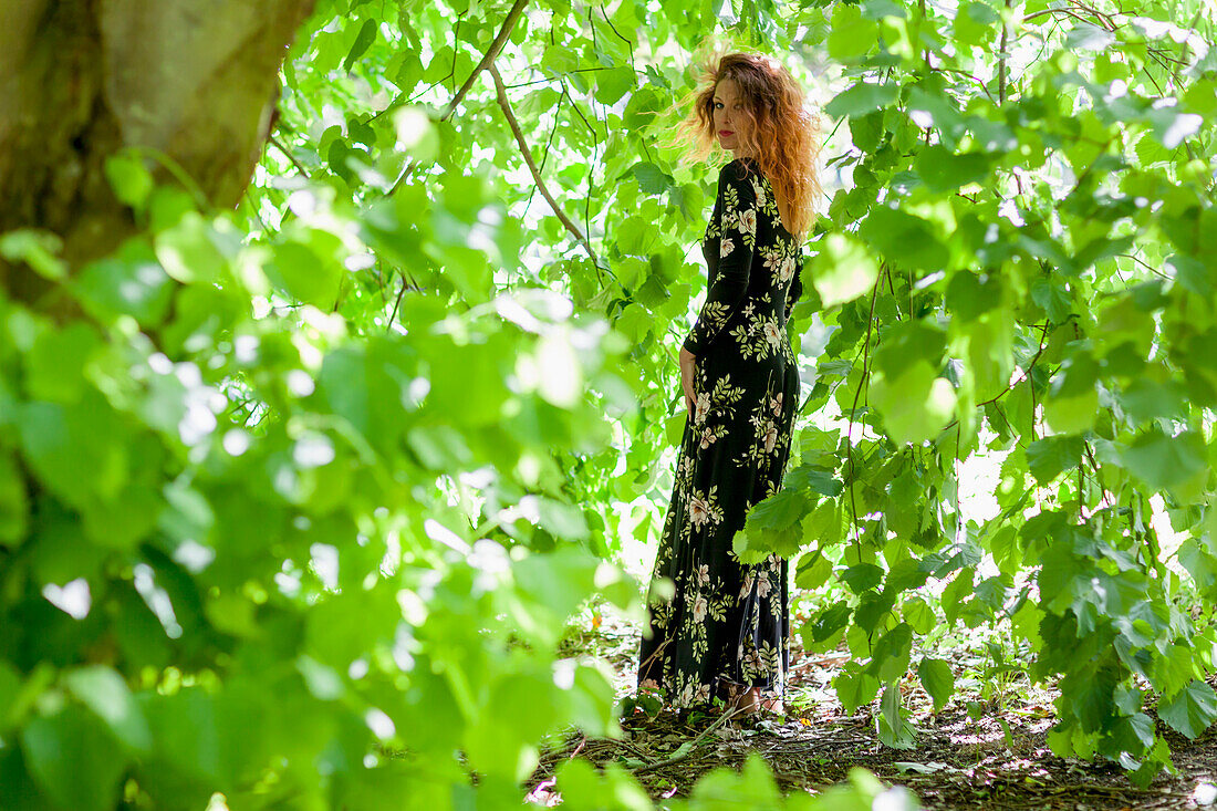 Woman in Floral Dress Standing amongst Leaves in Forest