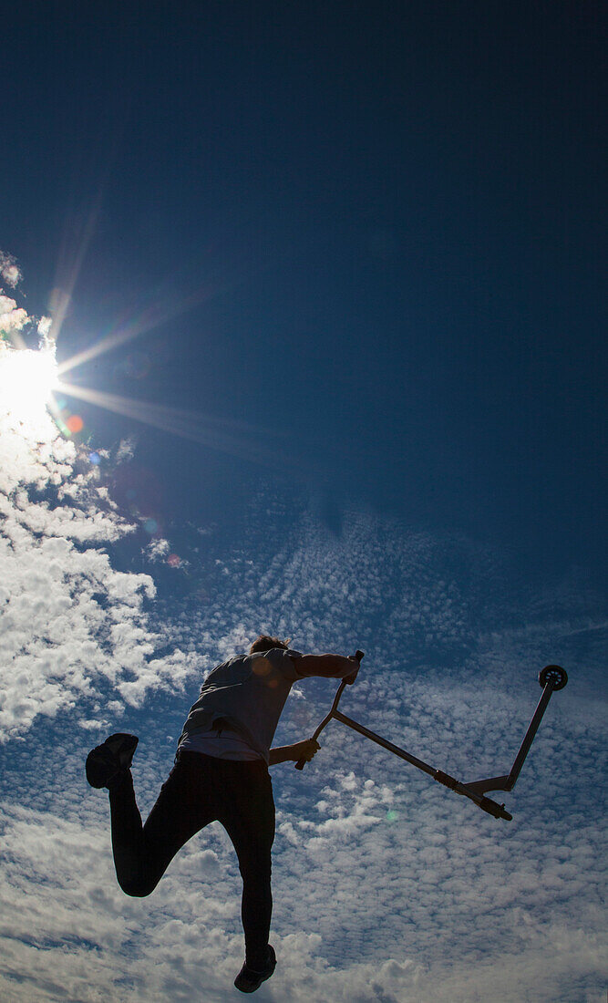 Skateboarder springt mitten in der Luft gegen Wolken und blauen Himmel