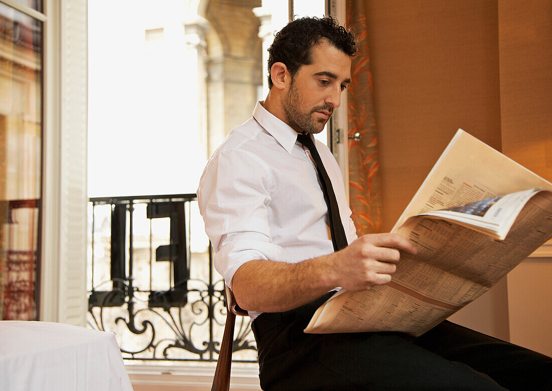 Businessman in hotel room reading newspaper