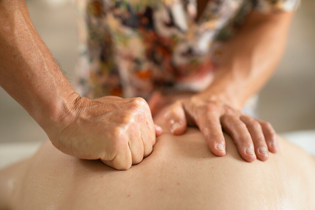 Nahaufnahme Massagetherapeutin massiert Rücken eines Mannes mit Faust