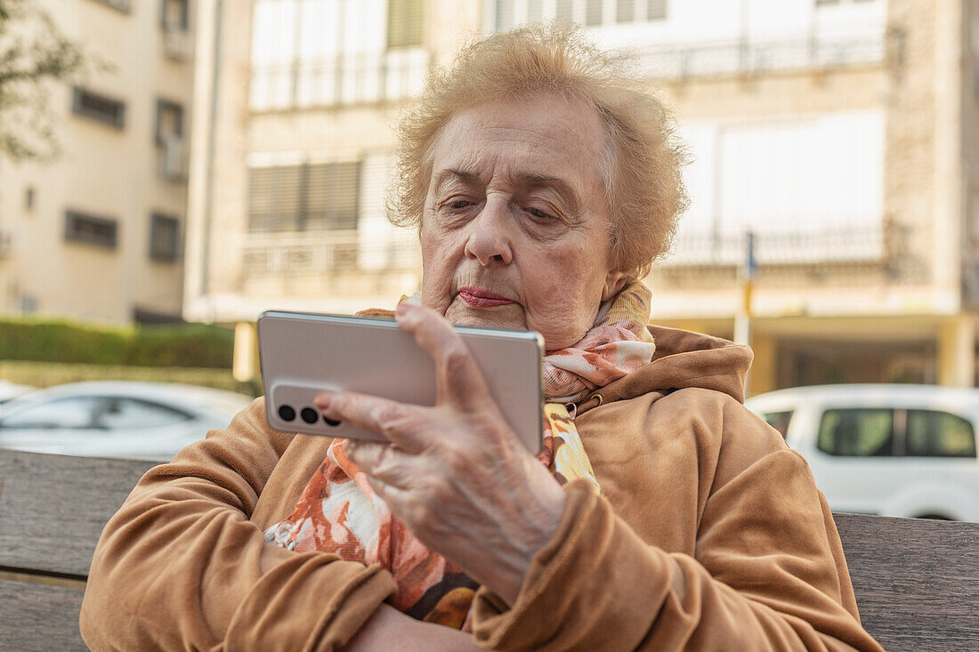 Ältere Frau sitzt auf einer Stadtbank und benutzt ihr Smartphone
