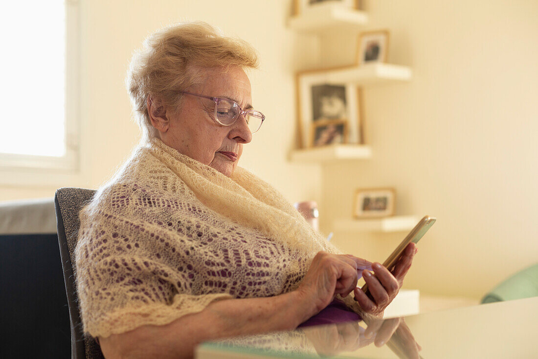 Ältere Frau mit Kopftuch benutzt Smartphone zu Hause