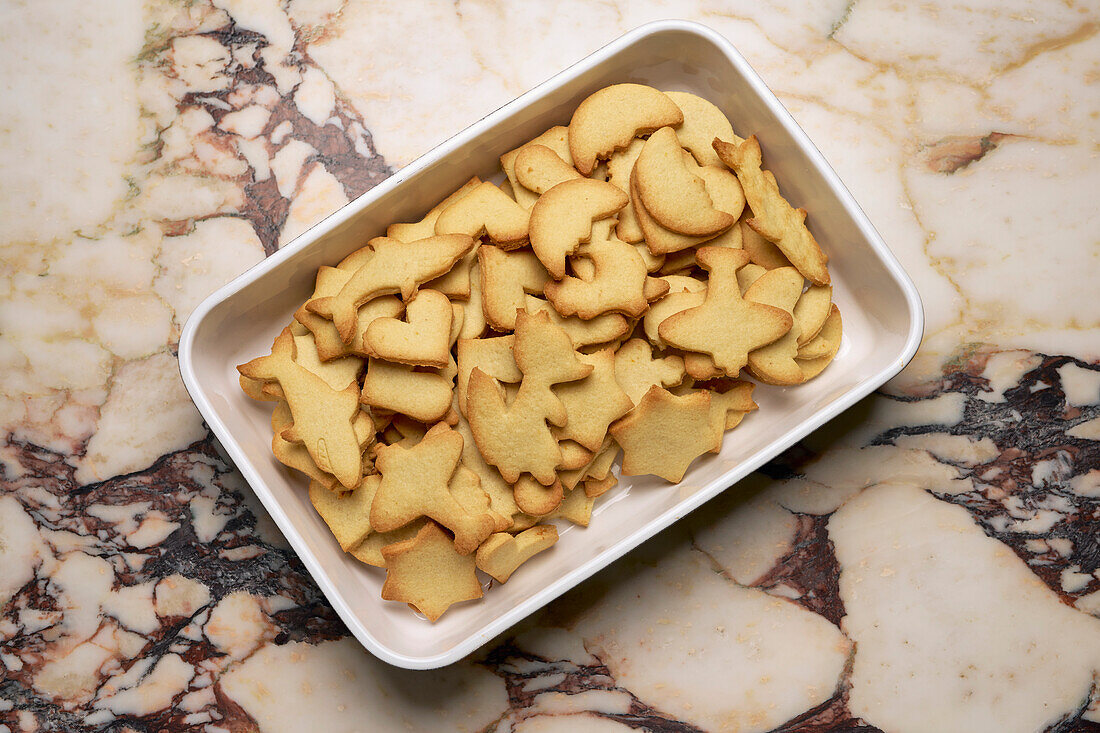 Blick von oben auf Zuckerplätzchen in verschiedenen Formen in einer Schale auf der Marmortheke