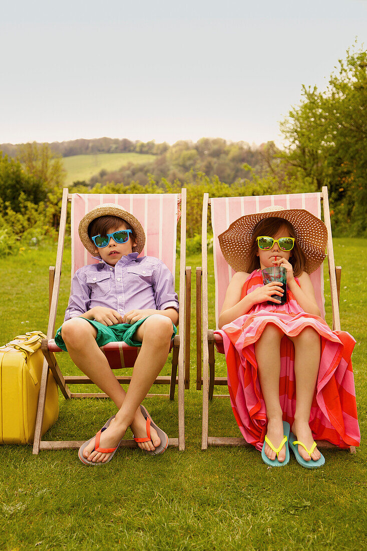 Junge und Mädchen mit Strohhut und Sonnenbrille auf einem Liegestuhl sitzend
