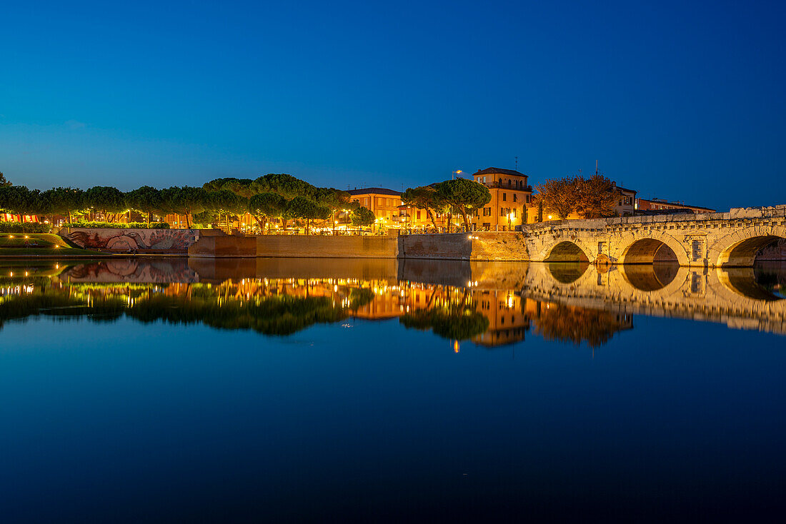 Blick auf die Ponte di Tiberio, die sich im Kanal von Rimini im Stadtteil Borgo San Giuliano in der Abenddämmerung spiegelt, Rimini, Emilia-Romagna, Italien, Europa