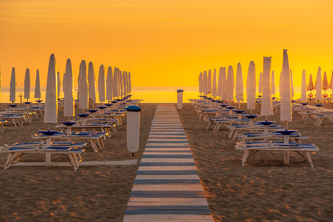 Blick auf Sonnenaufgang und Sonnenschirme am Lido am Strand von Rimini, Rimini, Emilia-Romagna, Italien, Europa
