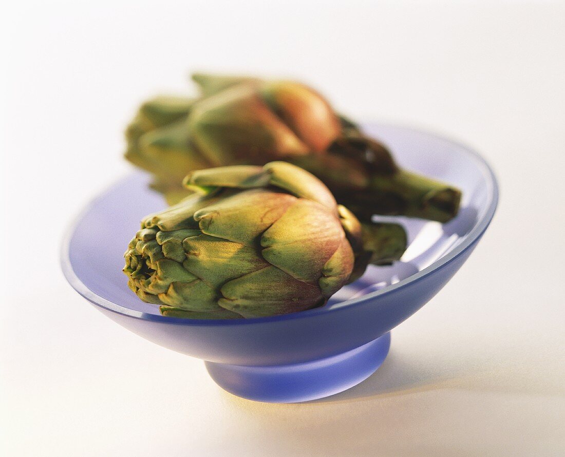 Two artichokes in pale-blue glass bowl