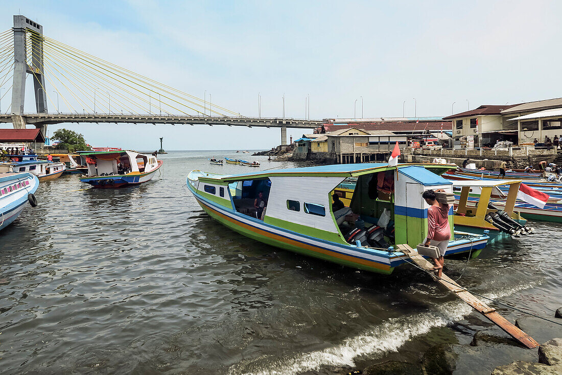 Covered ferry boats in Manado port with the Soekarno Bridge beyond in provincial capital of Sulawesi's far north, Manado, North Sulawesi, Indonesia, Southeast Asia, Asia