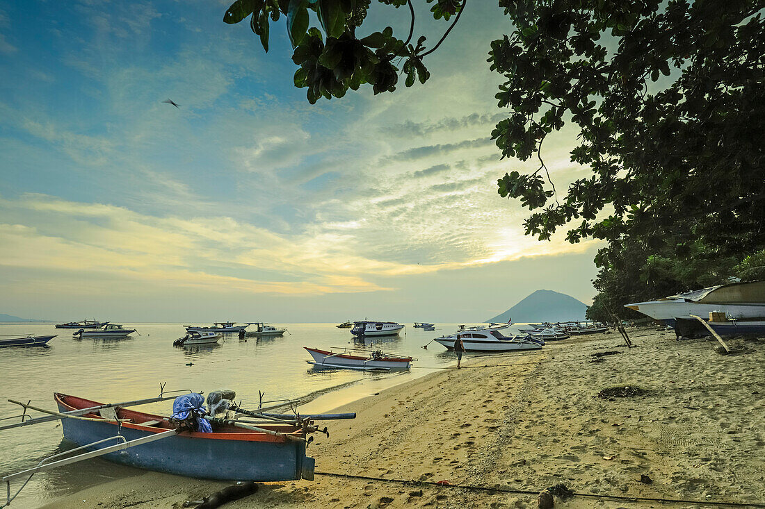 Boote vor dem Stadtstrand bei Sonnenuntergang mit der Insel Manadotua dahinter auf dieser Urlaubstauchinsel, Bunaken, Nordsulawesi, Indonesien, Südostasien, Asien