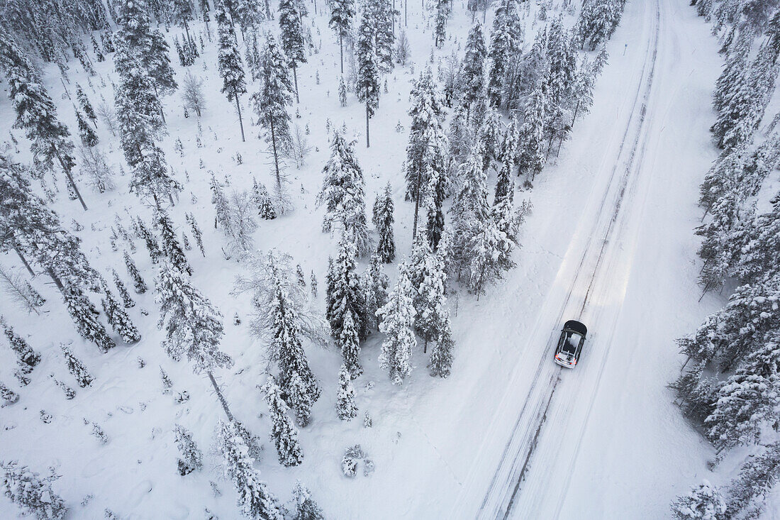 Luftaufnahme eines Autos, das auf einer vereisten Straße durch den schneebedeckten Wald fährt, Akaslompolo, Finnisch-Lappland, Finnland, Skandinavien, Europa