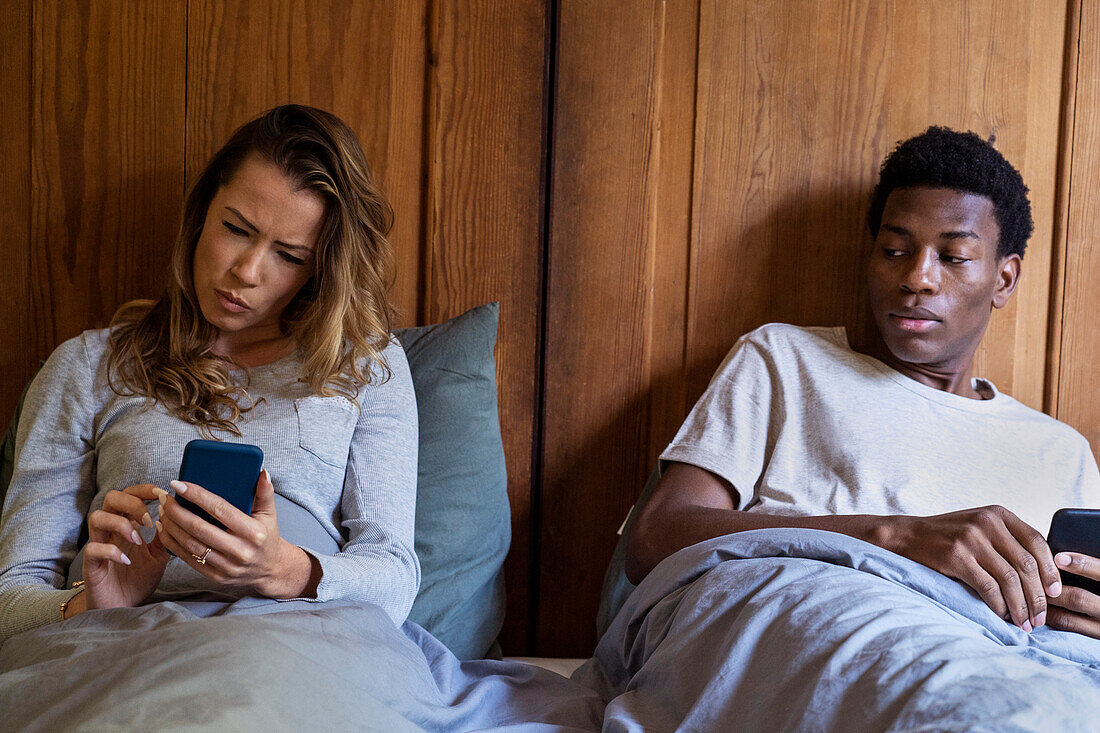 Misstrauischer Freund schaut auf das Smartphone seiner Freundin, während er im Bett liegt