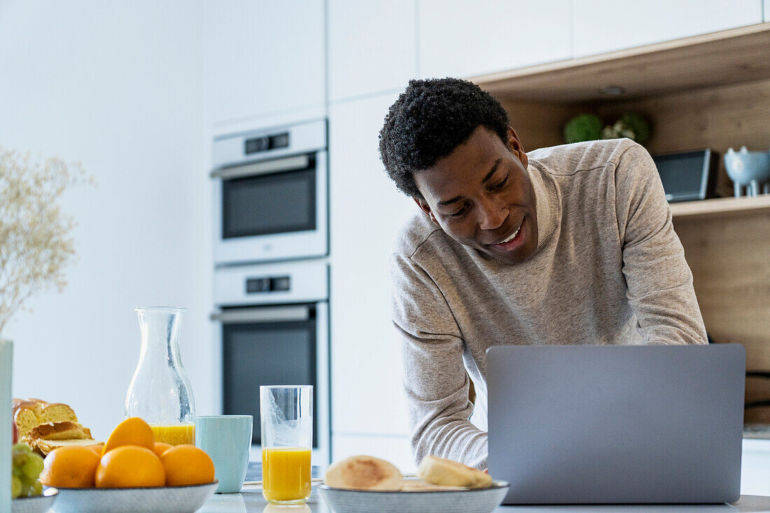 Adult man using laptop while leaning on kitchen counter