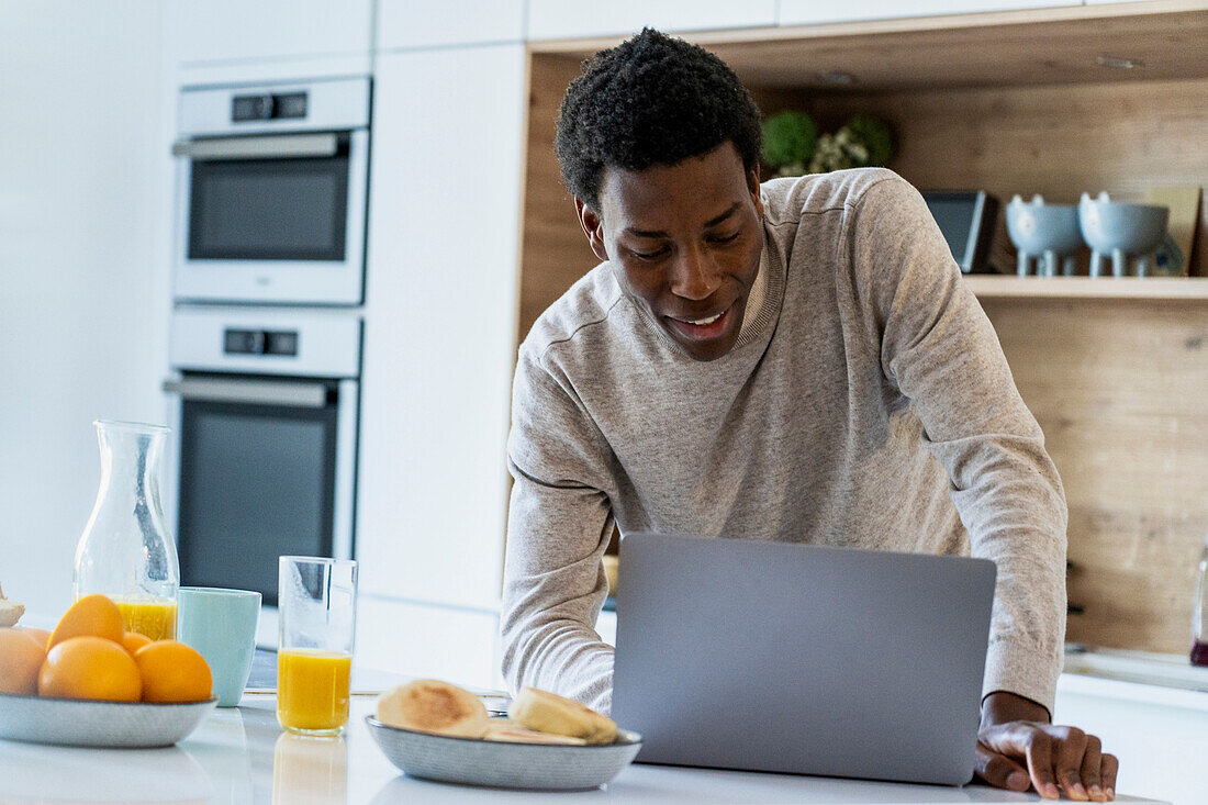 Erwachsener Mann benutzt Laptop, während er sich an den Küchentresen lehnt