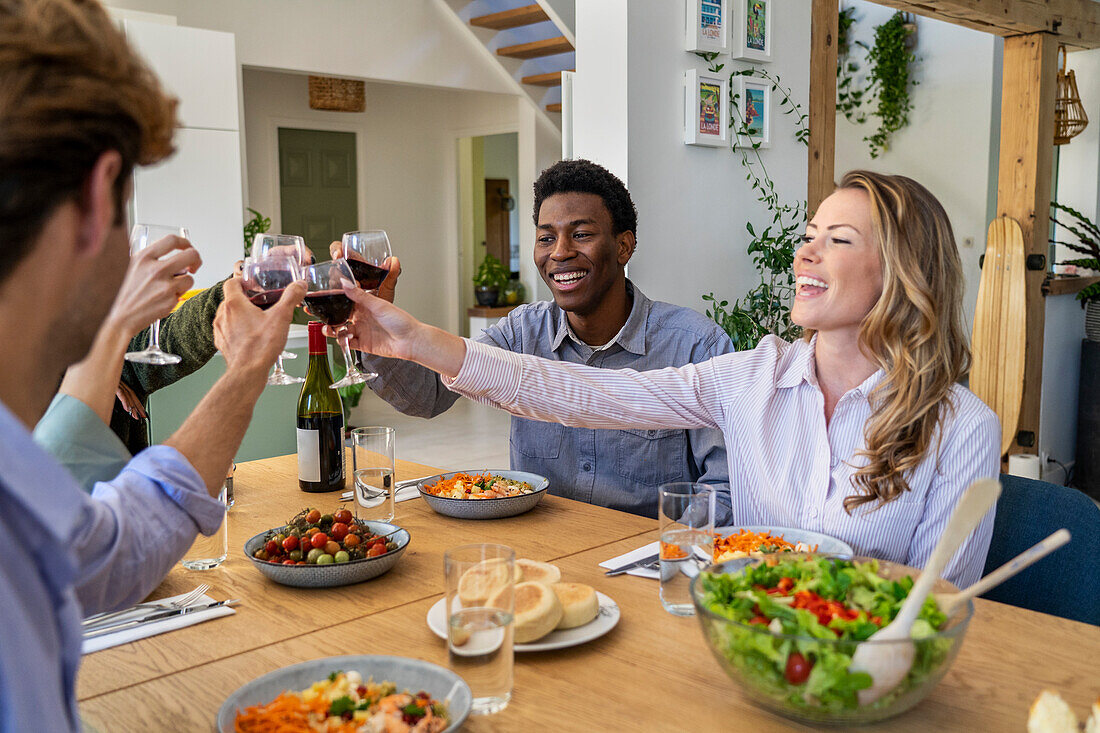 Group of friends toasting with wineglasses while having dinner in dinning room