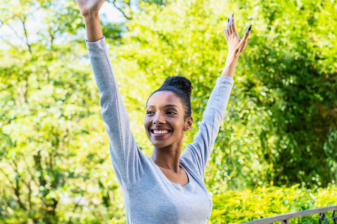 Cheerful young adult woman standing outdoors with arms raised