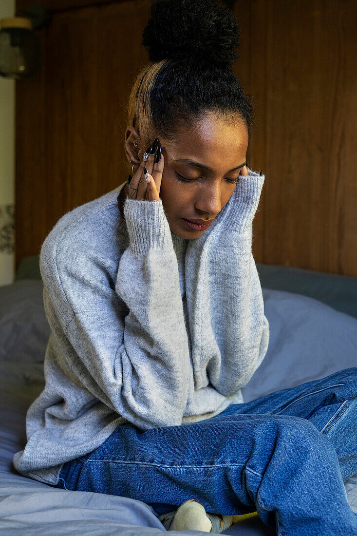 Stressed young adult woman touching her head while sitting on bed