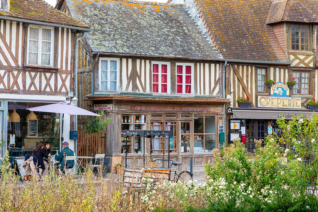 Touristen sitzen in einem Café in dem normannischen Dorf Beuvron-en-Auge, Beuvron-en-Auge, Normandie, Frankreich, Europa