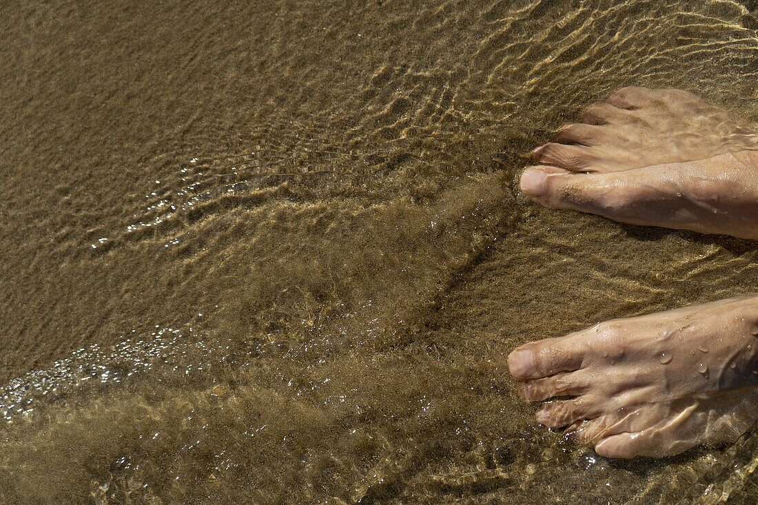 Füße einer nicht identifizierten Person im fließenden Wasser am Strand