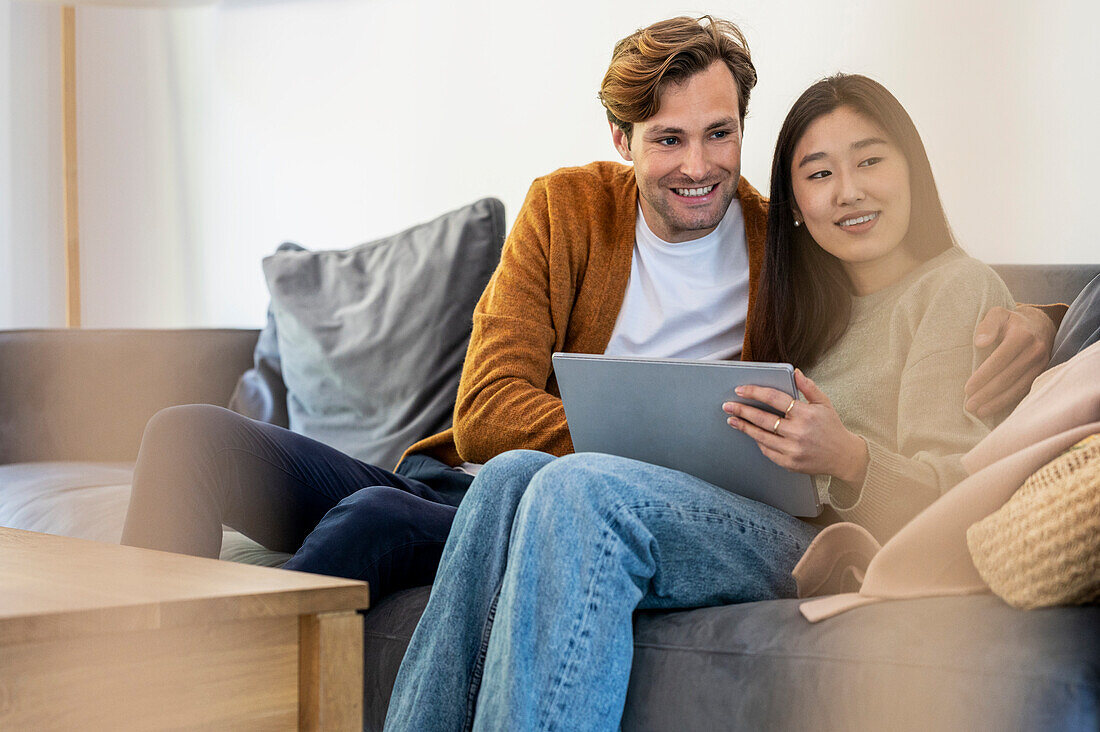 Adult couple using digital tablet while relaxing on sofa during daytime