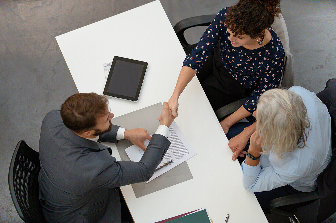 Adult couple shaking hands with lawyer after signing contract