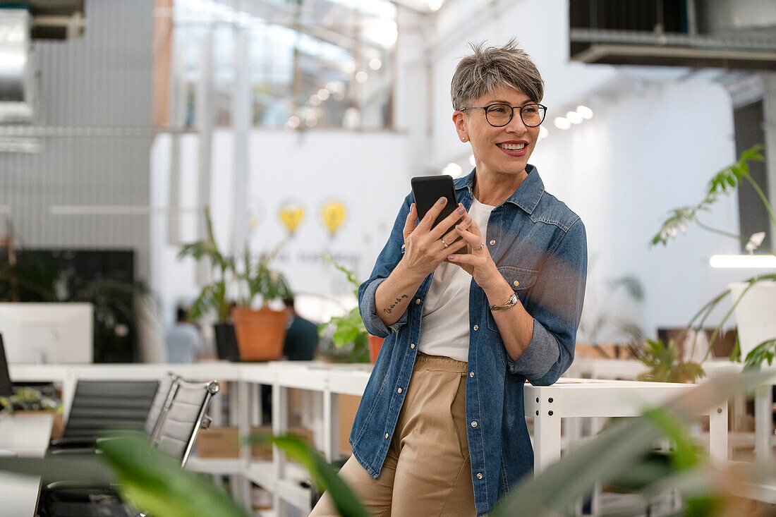 Female entrepreneur using smart phone while standing indoors