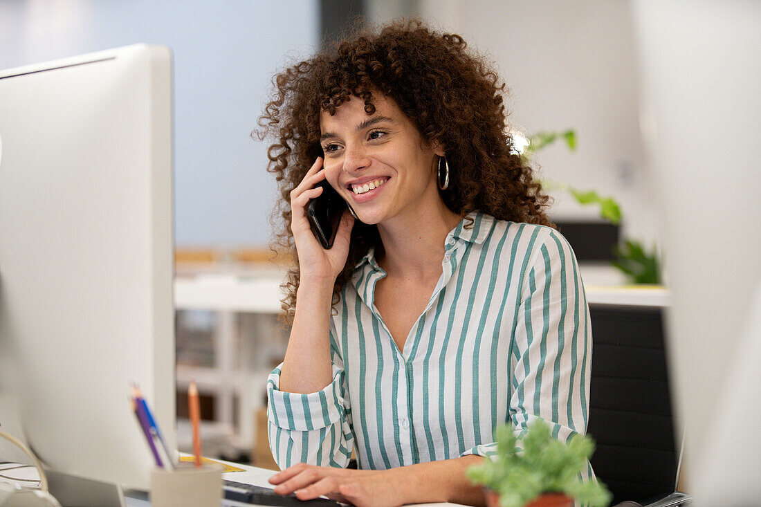 Young adult businesswoman talking on smart phone while working on computer