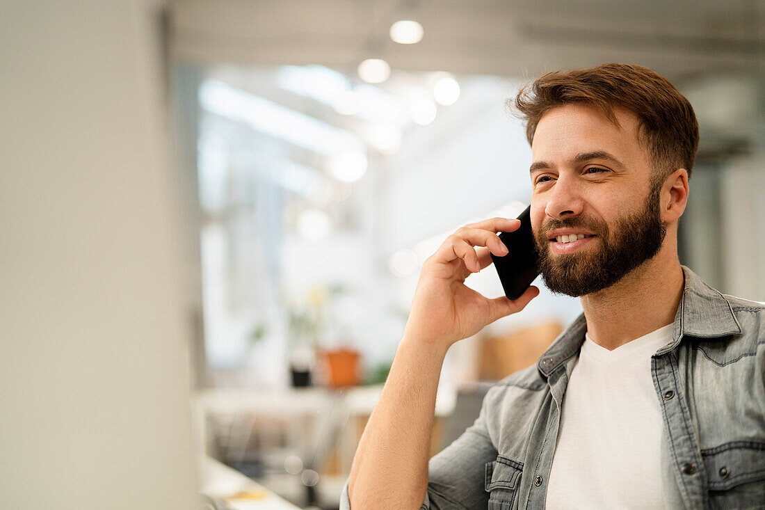 Male system engineer listening to voice mail while using computer