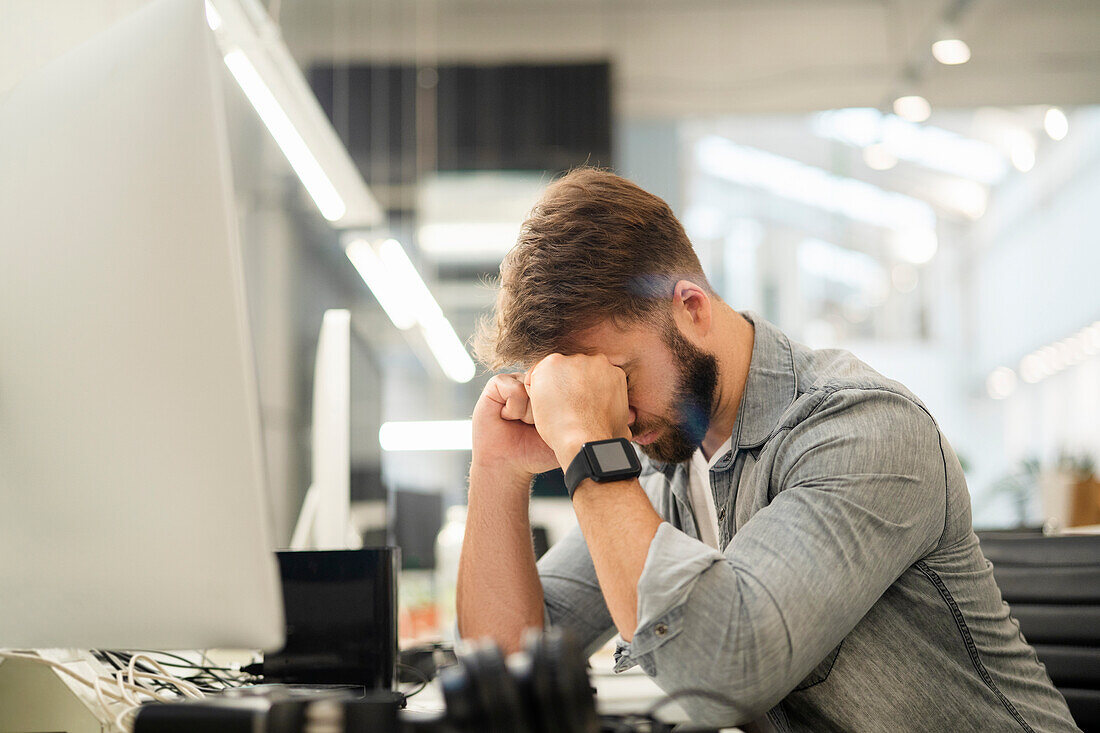 Stressed male entrepreneur sitting at desk while having a headache
