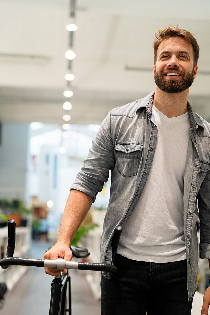 Männlicher Unternehmer verlässt sein Büro, während er mit dem Fahrrad an seiner Seite spazieren geht